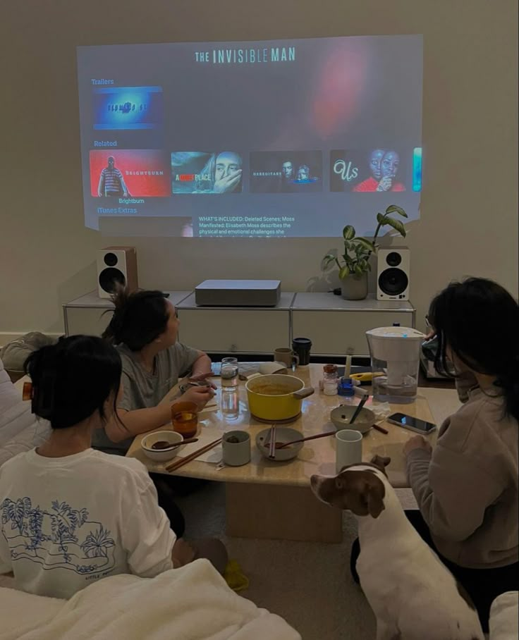 three people sitting at a table with food and drinks in front of a projector screen