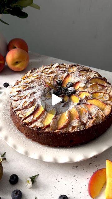 a cake sitting on top of a white plate next to sliced peaches and blueberries