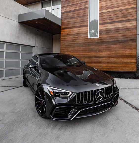 a black sports car is parked in front of a house with wood siding on the side