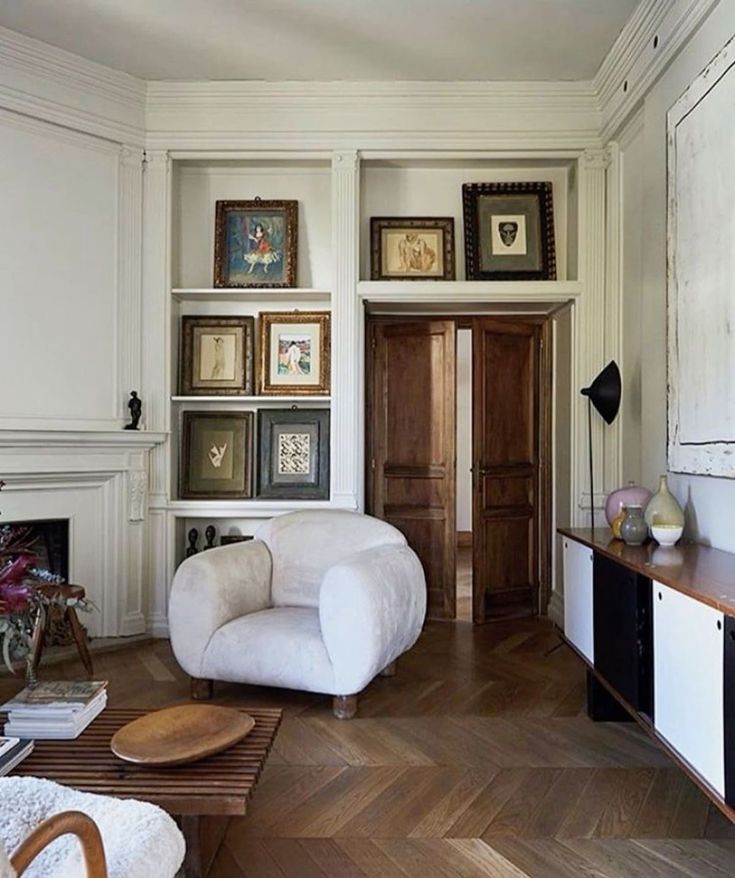 a living room filled with white furniture and pictures on the wall above it's fireplace