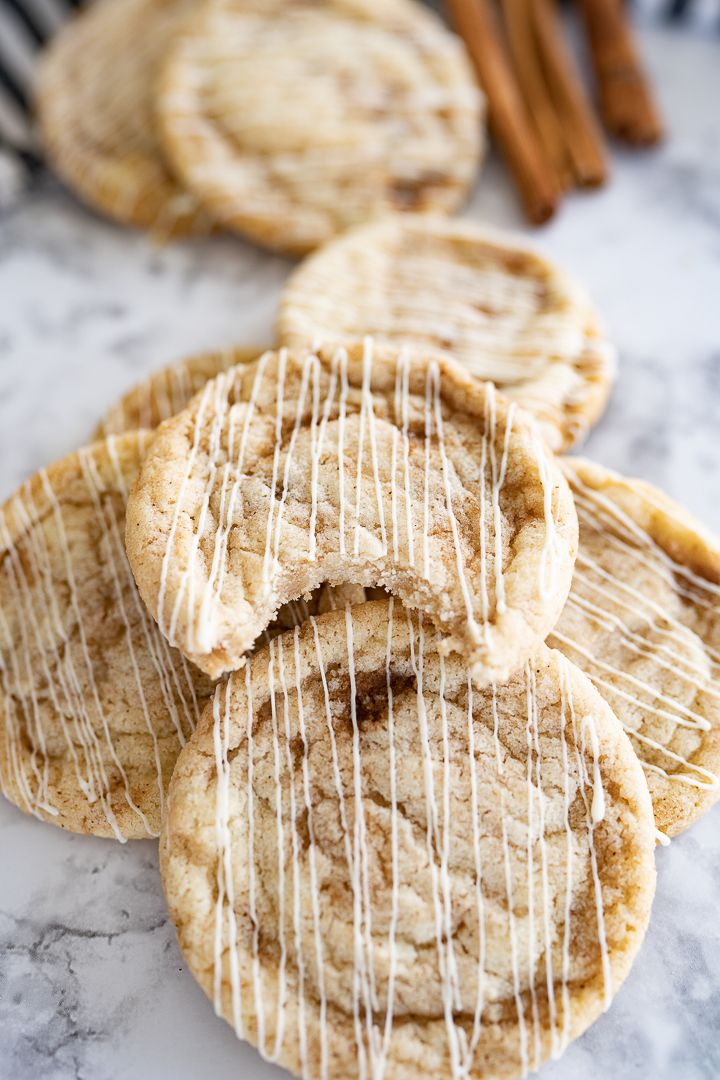 cinnamon sugar cookies drizzled with icing on a marble countertop next to cinnamon sticks