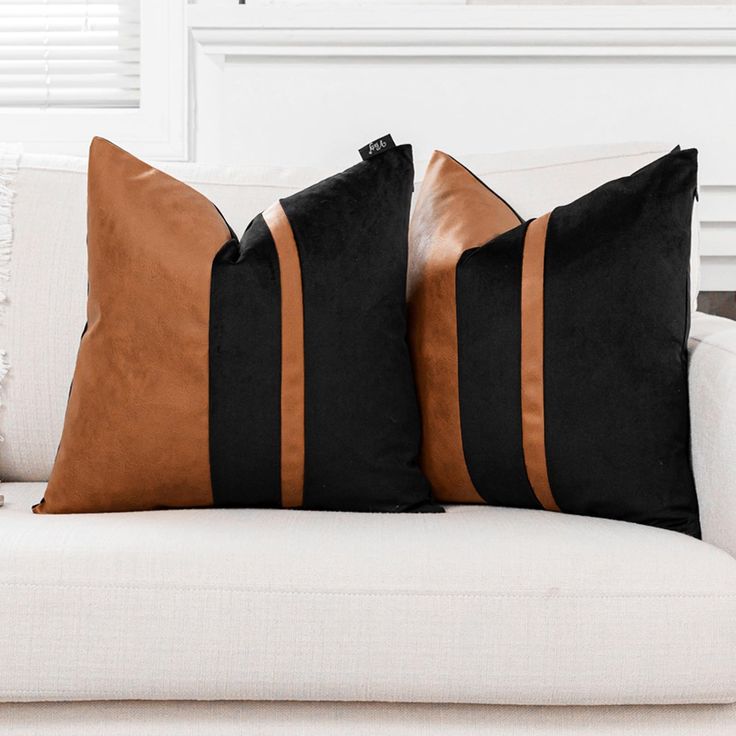 two black and brown pillows sitting on top of a white couch