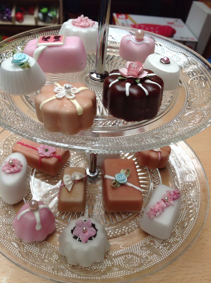 there are many different types of cakes on the glass platter and one is decorated with fondant