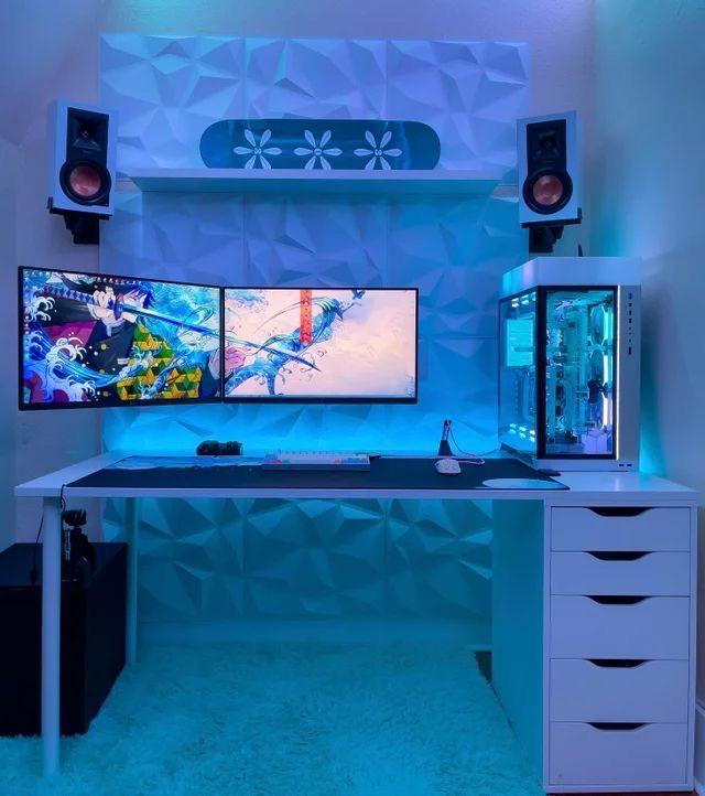 a computer desk with two monitors and speakers on it in front of a blue wall