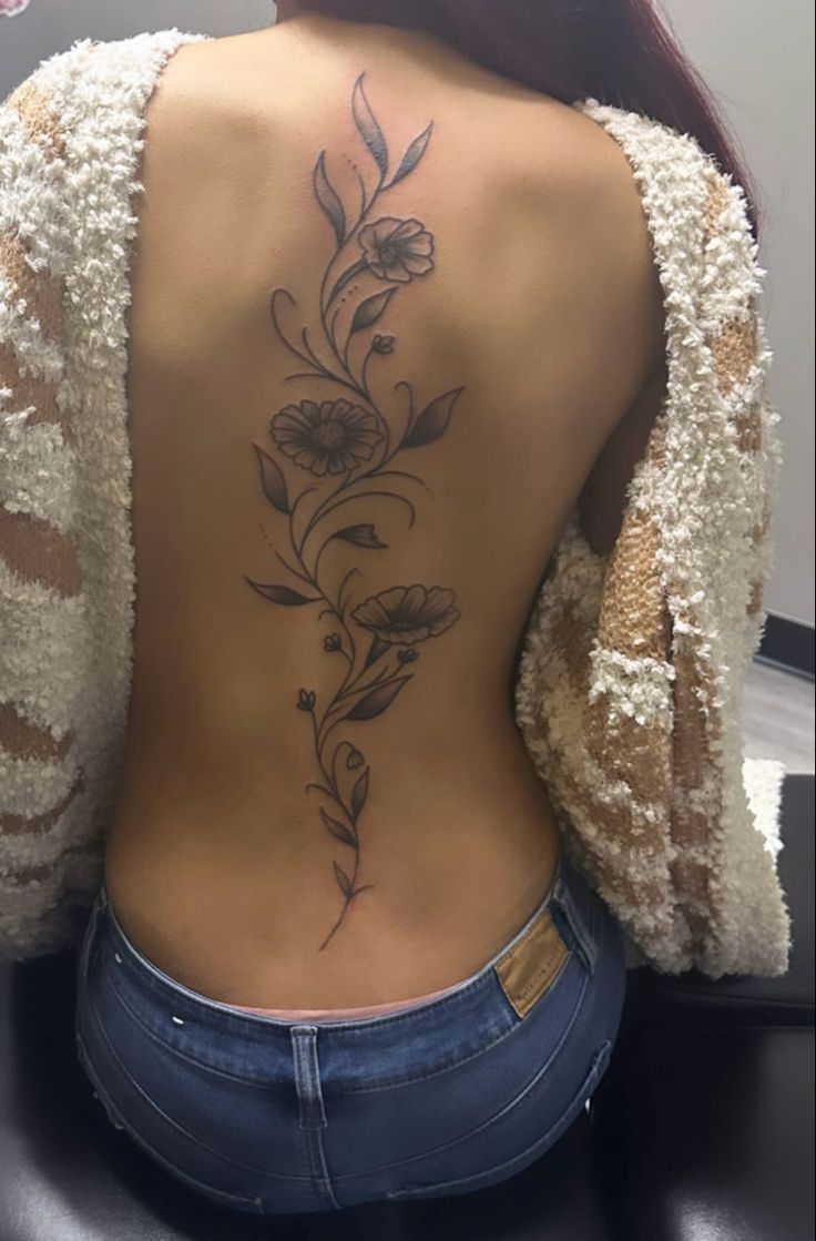 the back of a woman's body with flowers tattooed on her upper and lower back