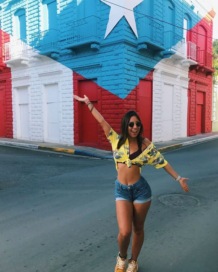 a woman riding a skateboard down a street next to a large building with red, white and blue painted walls