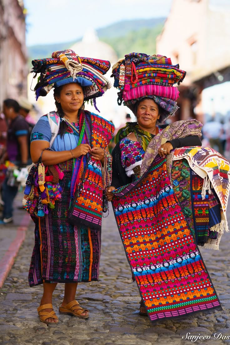 two women in colorful clothing are standing on the cobblestone street with their heads wrapped around each other