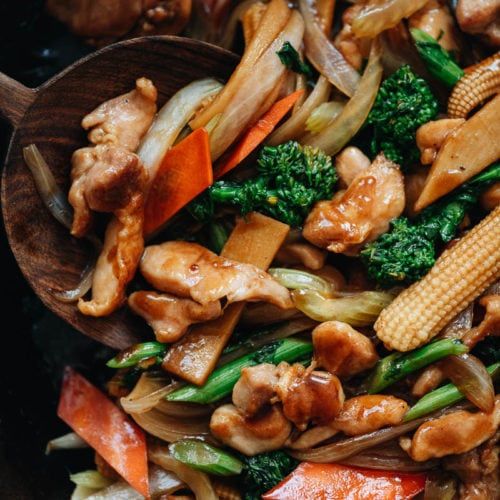 stir fry with chicken, broccoli, carrots and corn in a wooden spoon