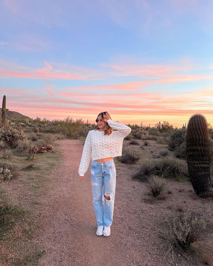 a woman standing on a dirt road next to a cactus