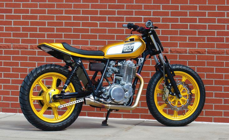 a yellow and black motorcycle parked in front of a brick wall