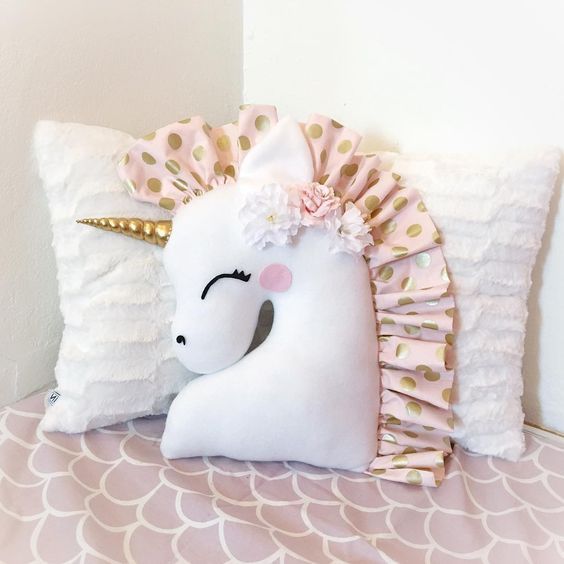 a white pillow with a pink and gold unicorn on it's side sitting on a bed