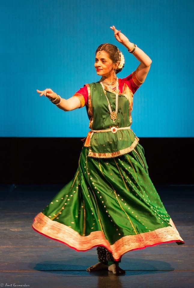 a woman in a green and red dress is doing something with her hands while standing on a stage