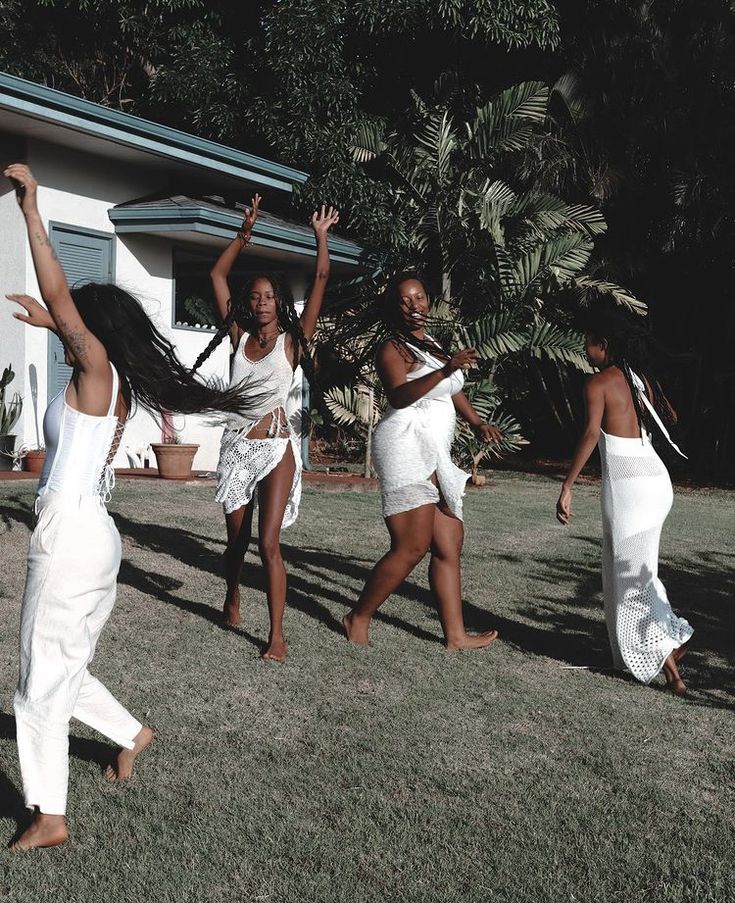 four women in white dresses are dancing on the grass