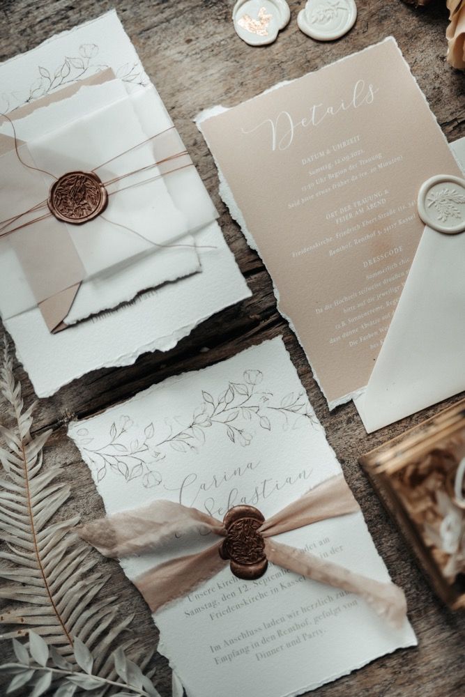 the wedding stationery is laid out on top of each other, with buttons and ribbons