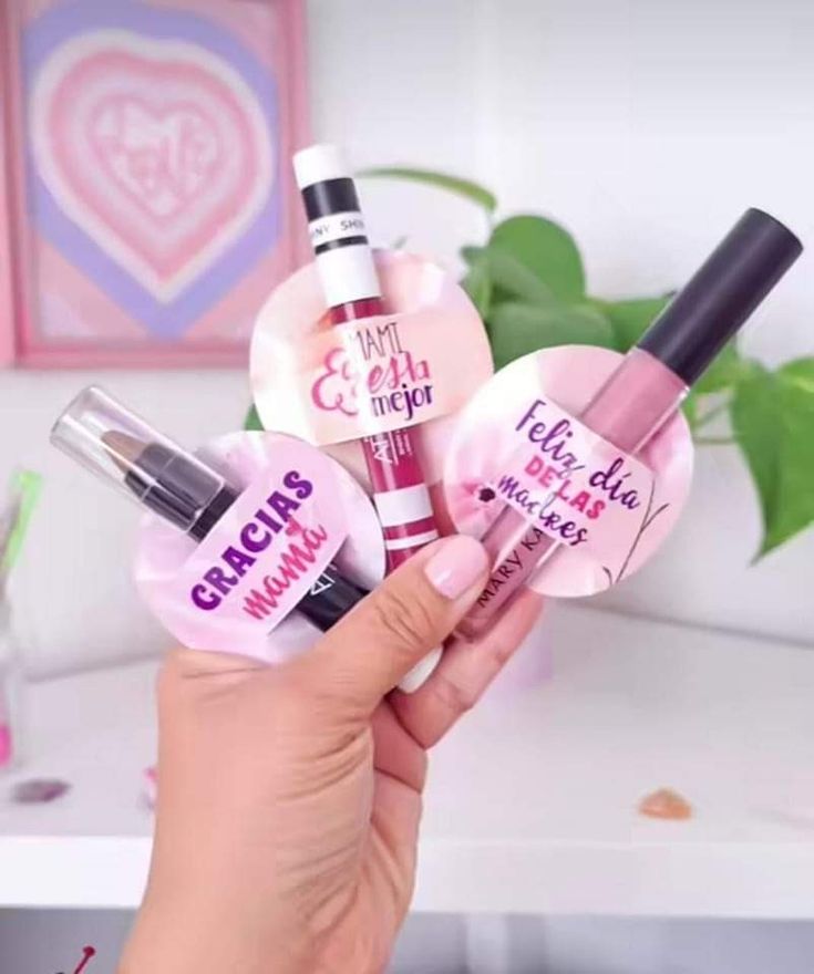 three lip glosses in the shape of heart shaped bottles with pink lettering on them