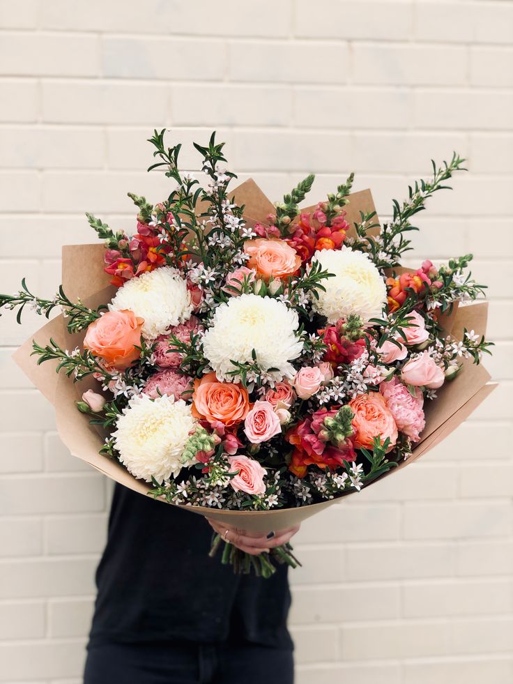 a person holding a bouquet of flowers in front of a brick wall