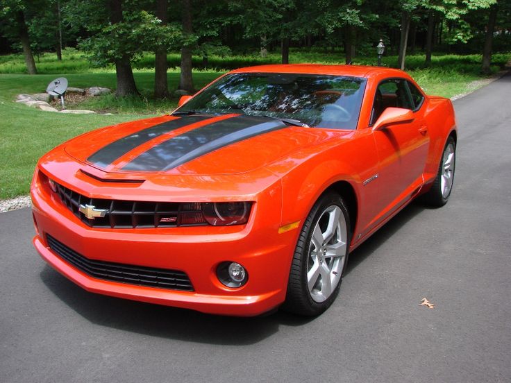 an orange sports car is parked on the side of the road in front of some trees