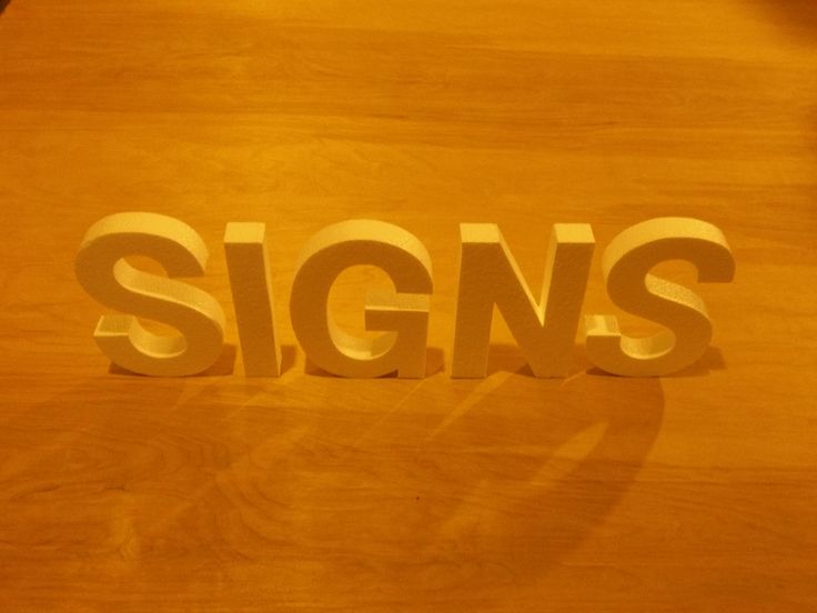 the word signs is cut out of wood and placed on top of a wooden table