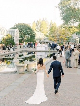 a bride and groom holding hands while walking in front of a pond at their wedding