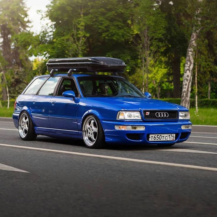 the blue car is parked on the side of the road with its roof rack strapped to it's trunk