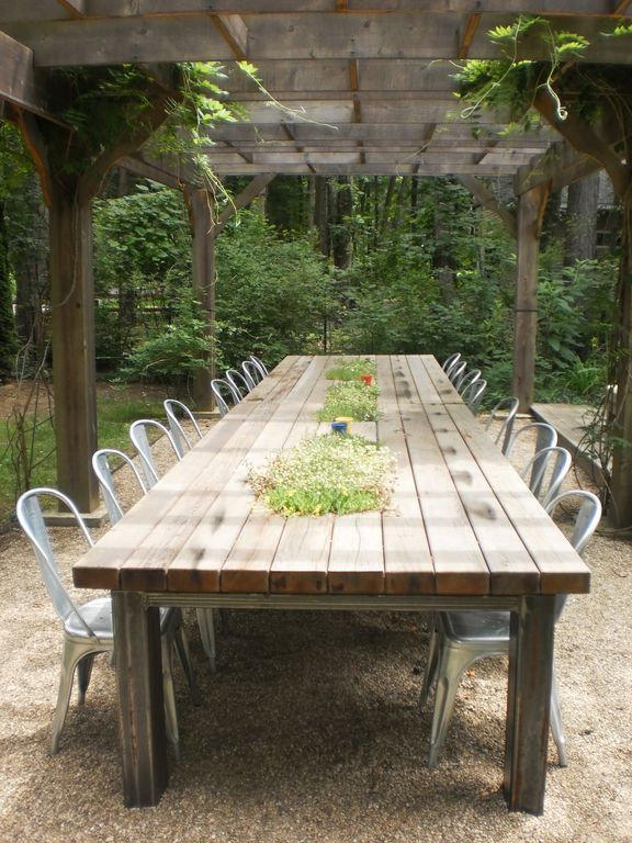 a wooden table with chairs around it under a pergolated area in the woods