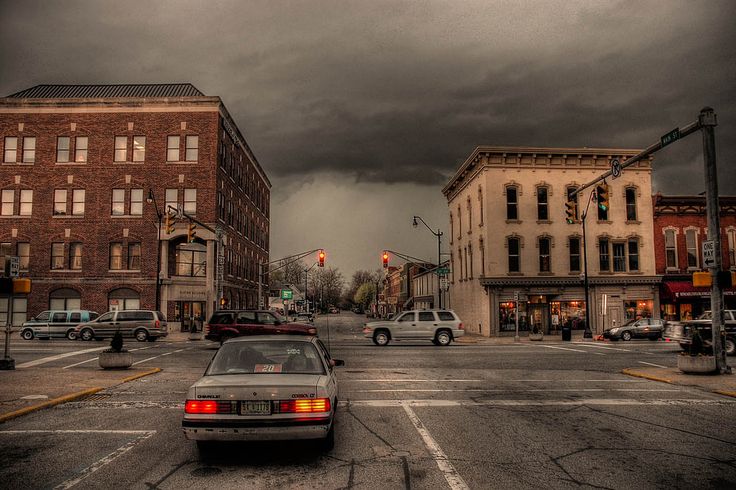 cars are stopped at an intersection in the city on a cloudy day with dark clouds overhead