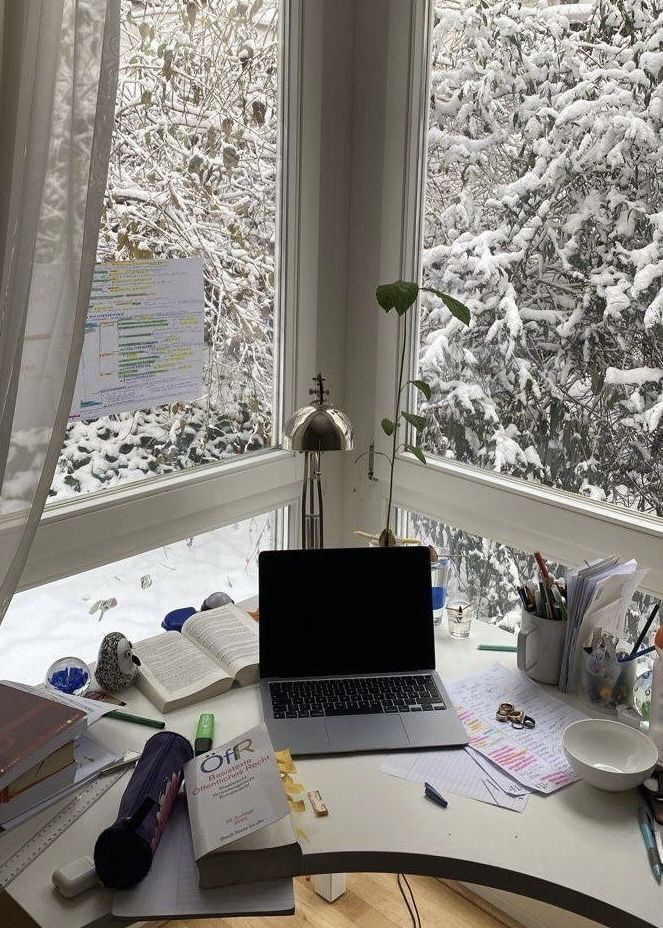 a laptop computer sitting on top of a desk in front of a window covered in snow