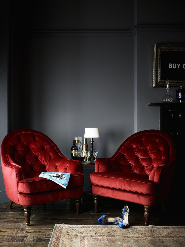 two red chairs sitting next to each other on top of a wooden floor in front of a gray wall