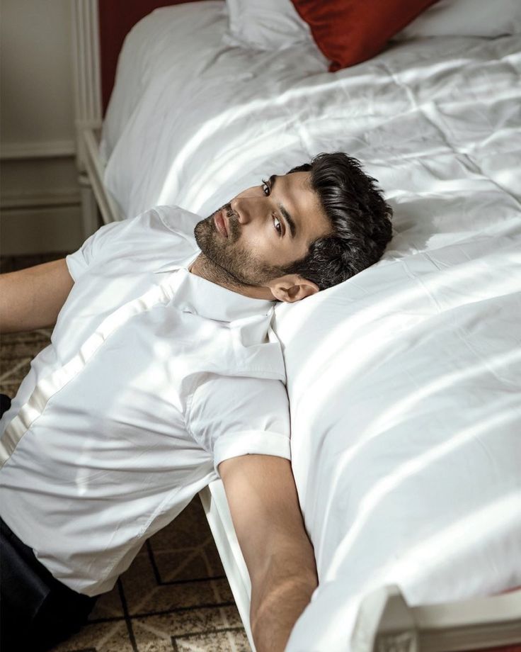 a man laying on top of a bed next to a red pillow and white sheets