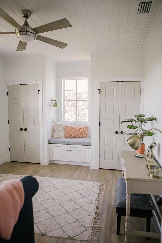 a living room with white walls and wood flooring, a window seat on the far wall