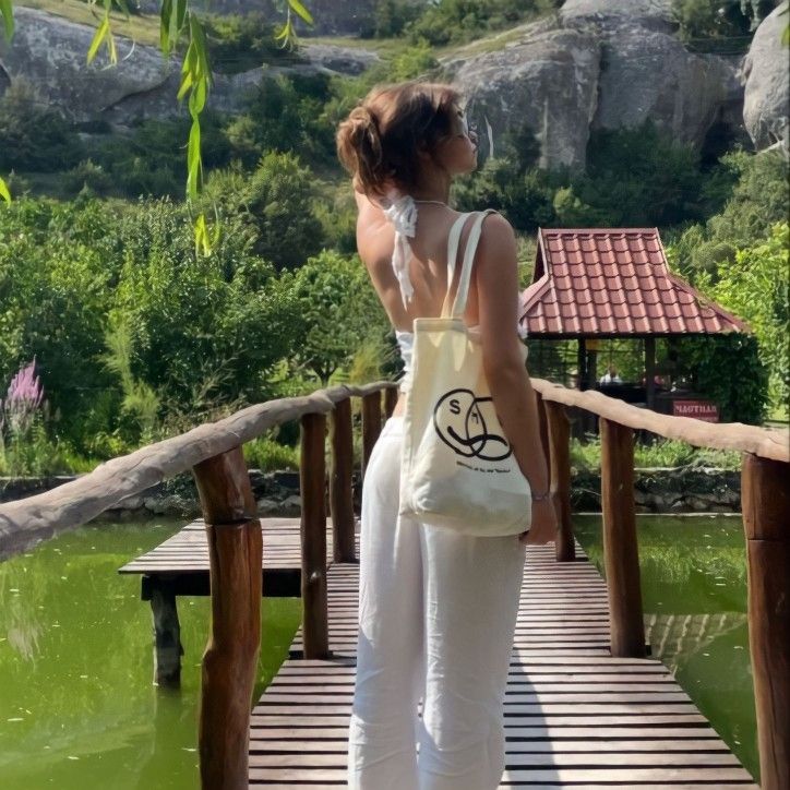 a woman is standing on a bridge with a bag in her hand and looking at the water