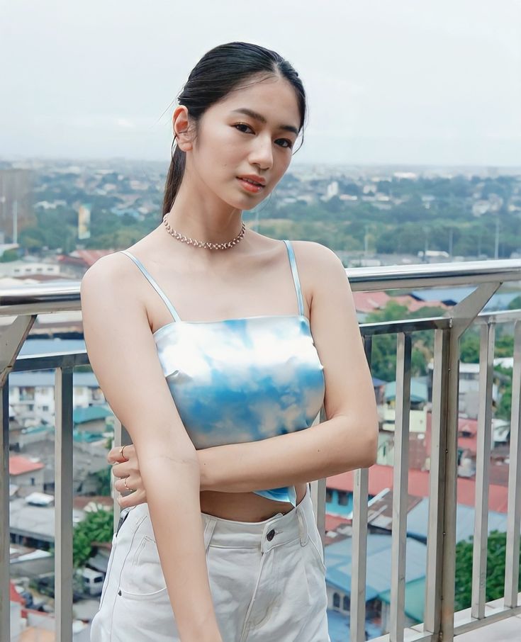 a young woman standing on top of a balcony next to a railing with buildings in the background