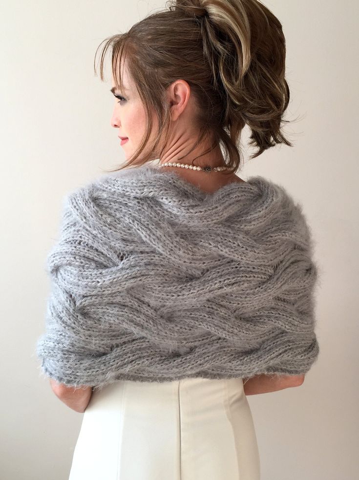 a woman wearing a gray knitted shawl over her shoulder and white pants, looking off to the side