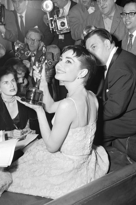 a black and white photo of a woman holding an award in front of a group of people