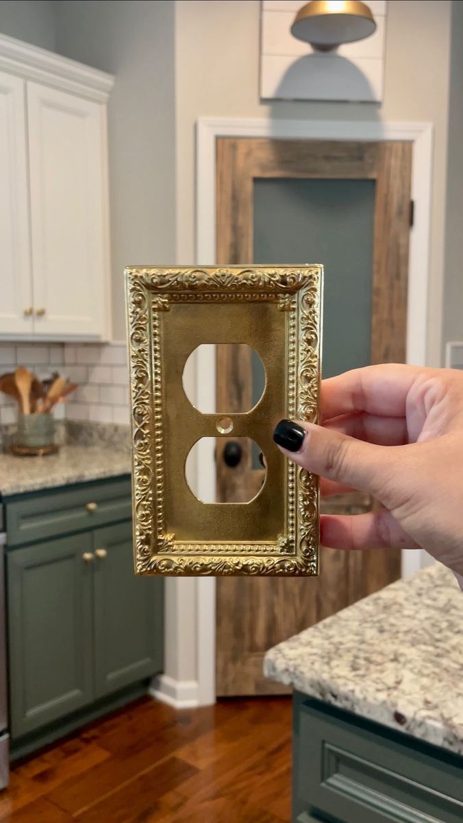 a person is holding up a gold light switch cover in the kitchen with granite counter tops