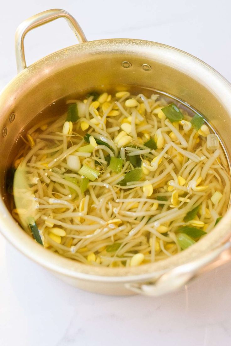 a pot filled with noodles and vegetables on top of a white countertop next to a spoon