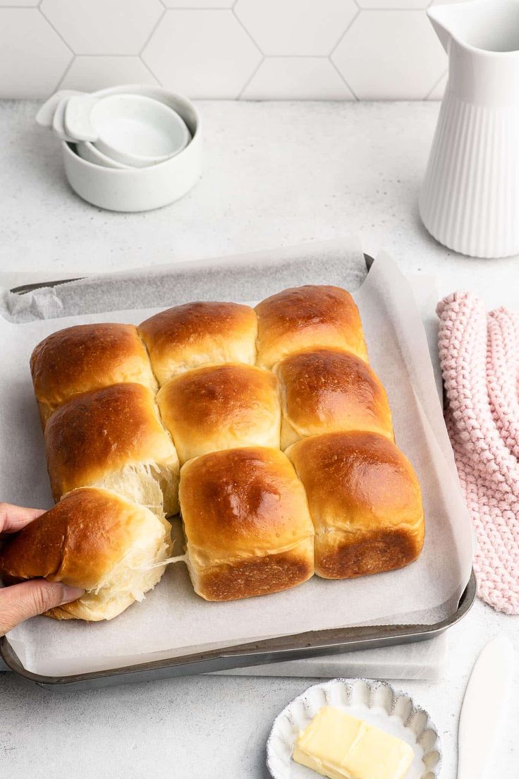 a person is holding a piece of bread on a baking sheet with butter in the background