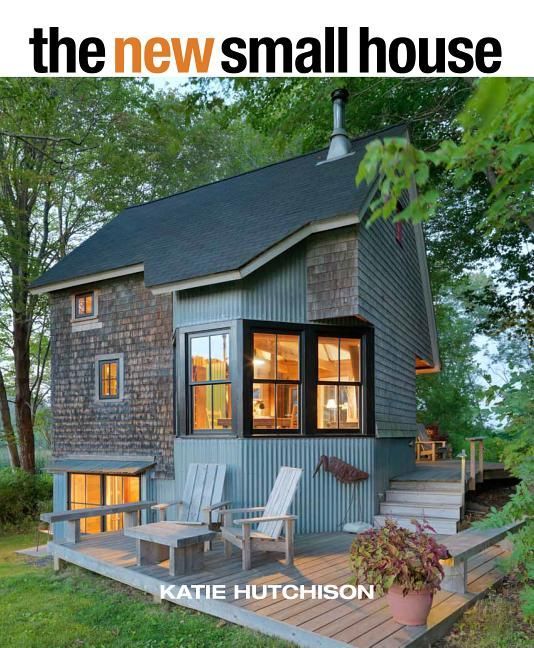 a small house with a deck and chairs on the front porch, surrounded by trees