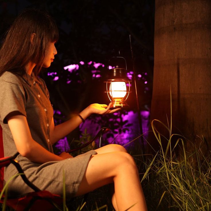 a woman sitting in a chair with a lantern on her hand and looking at it