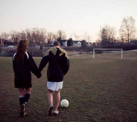 two girls are holding hands and walking towards a soccer ball