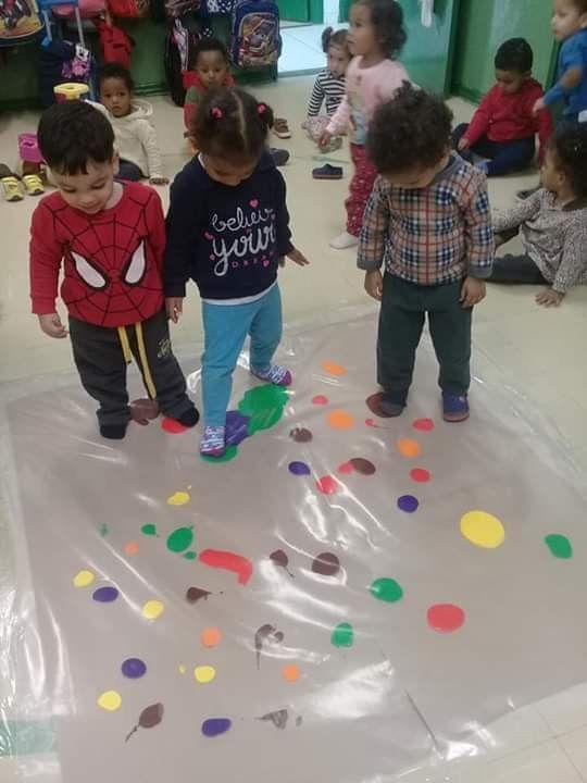 several children are standing on a sheet of plastic in a room with many other kids