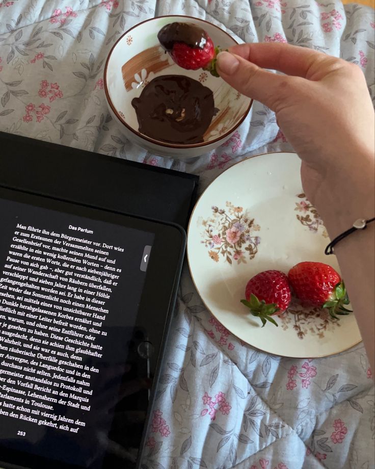 a person is eating strawberries and reading a book on the bed with their tablet