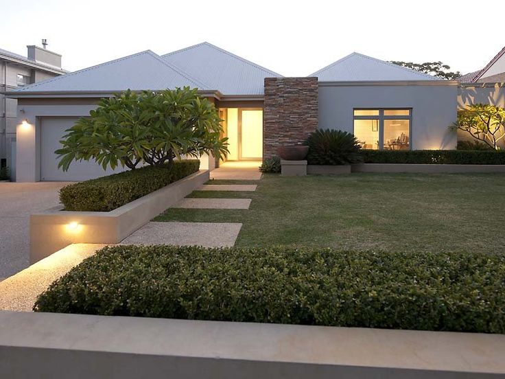 a modern house is lit up at night with lights on the front lawn and landscaping