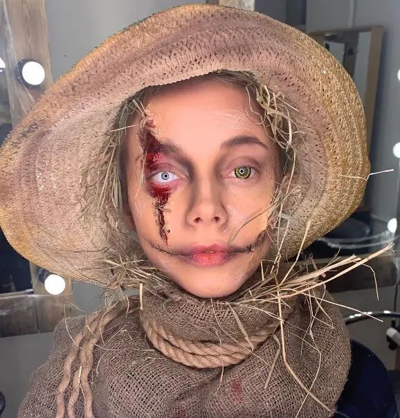 a woman wearing a straw hat with blood all over her face and nose, standing in front of a mirror