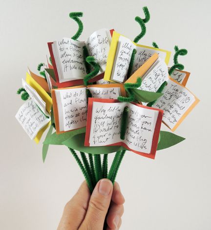 a hand holding an origami book bouquet made out of folded books with writing on them