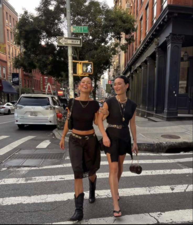 two women walking down the street in front of a crosswalk with cars behind them