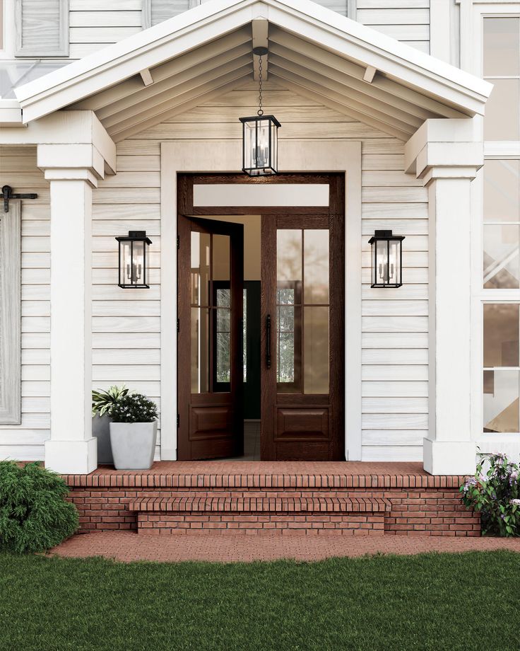 the front door of a white house with two potted plants on the steps and windows