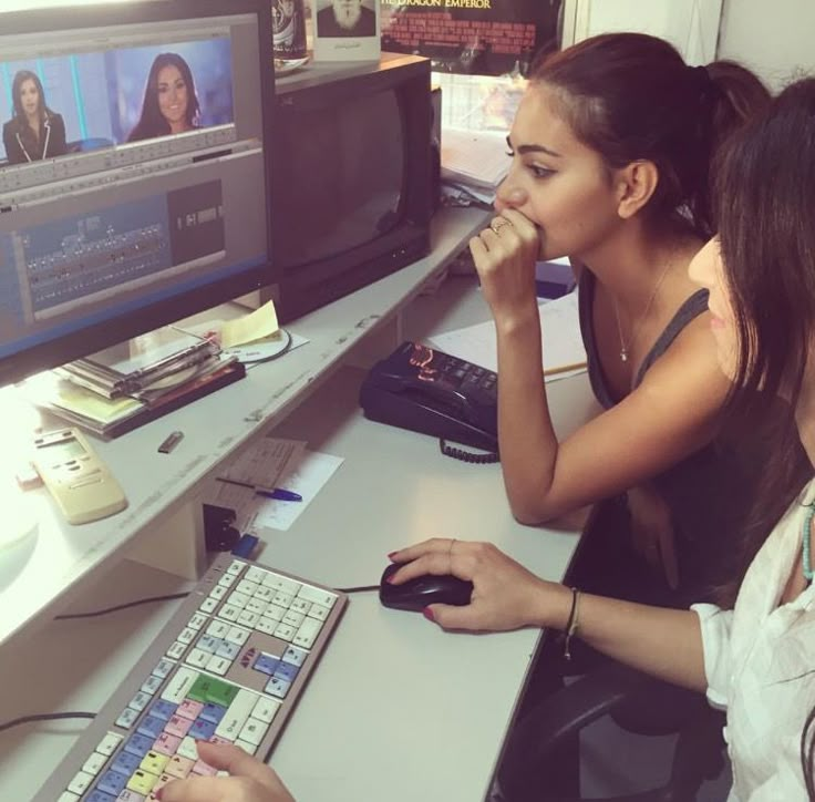 two women sitting at a desk with computer equipment