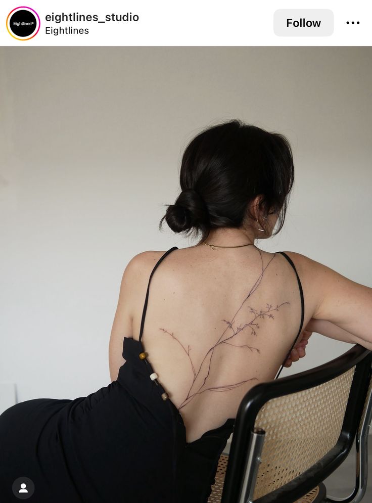 a woman sitting in a chair with her back turned to the camera and tattoos on her chest