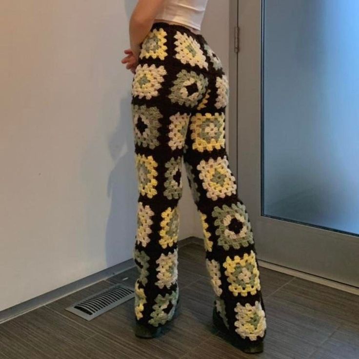 a woman standing in front of a wall with her back to the camera and wearing floral pants